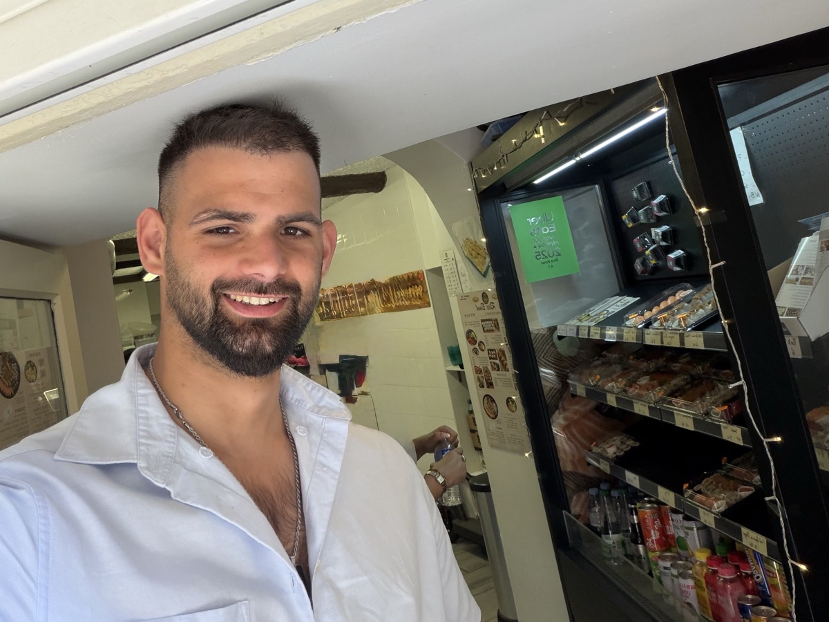 Denis, smiling in a light blue shirt in the shop doorway